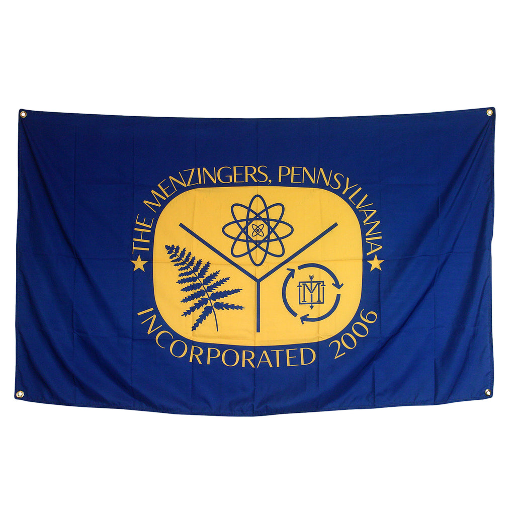image of navy blue wall flag on white background. flag has 4 brass grommets on each corner to hang it up and has a middle print in yellow that says, the menzingers, pennsylvania arched on top, incorporated 2006 arched on bottom. in beween the words is an image of fern leaves, an eight sided star like enery symbol, and an arrow circle recycling symbol with an emblem of an M with an arrow down the middle in the middle of the circle arrows. 