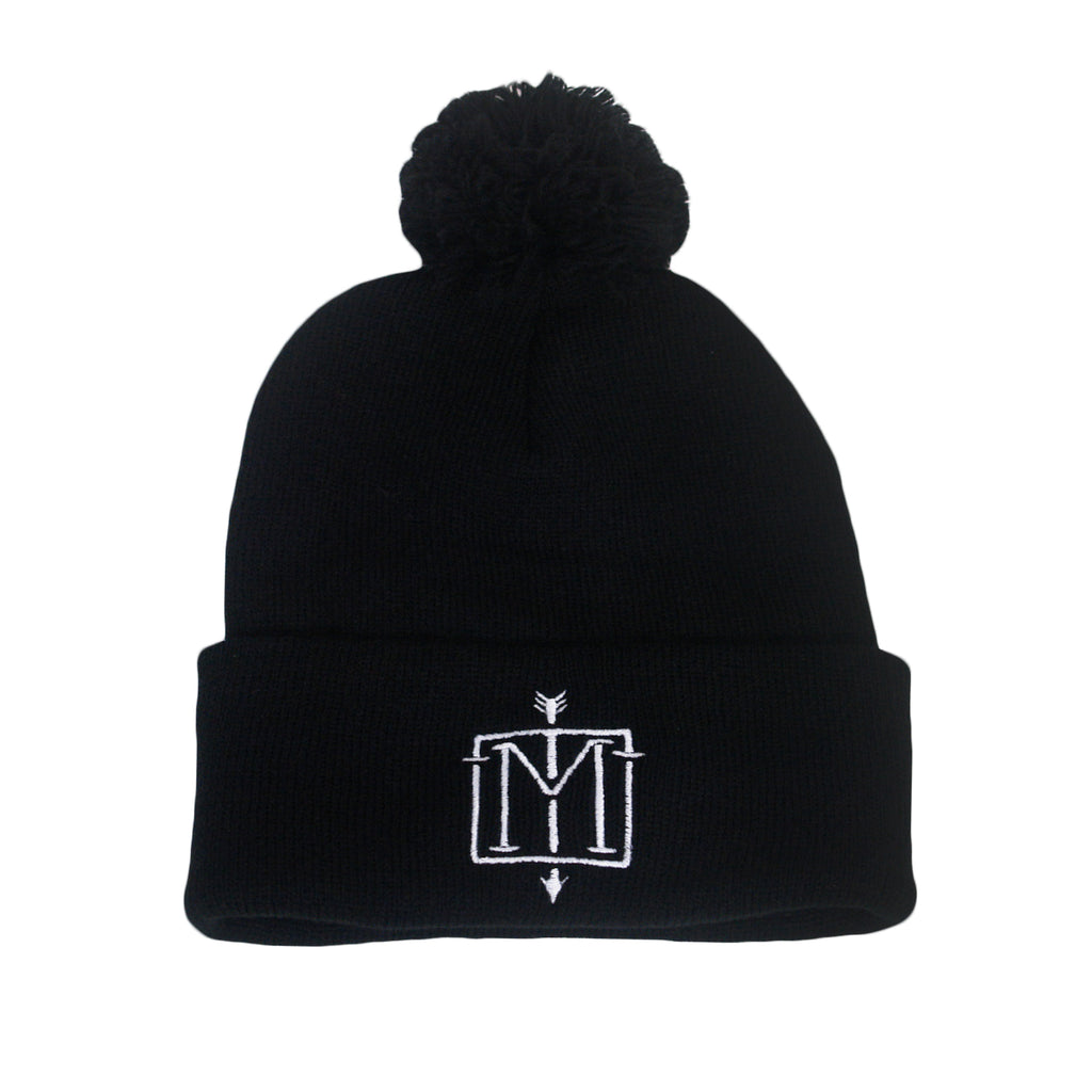 image of black winter pom beanie on white background. top of beanie has puff ball and the cuff of the beanie has in the center a white embroiderd emblem M with an arrow down the center. 