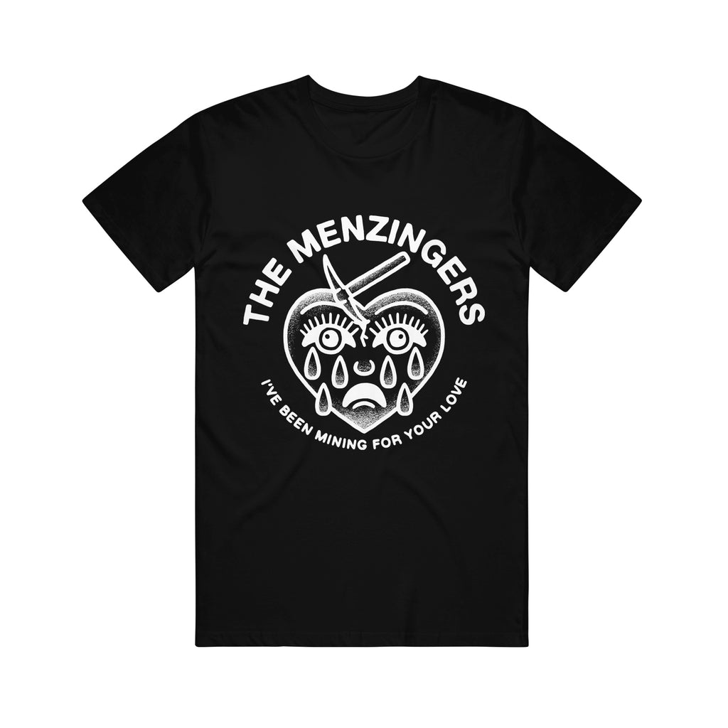 black tee shirt on white background. tee has full chest print in white on the front that has arched text that says the menzingers on the top and arched up text below that says i've been mining for your love. between the text is a drawing in white of a heart with a face that has a spike in the top left of the head and tears down the face.